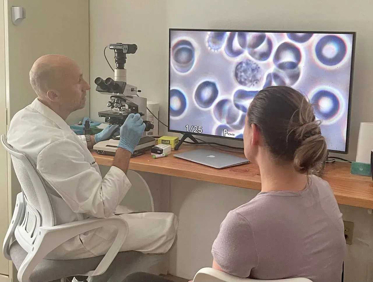 Др Никольский разъясняет пациентке состояние её крови, изображение с микроскопа транслируется на экран компьютера
