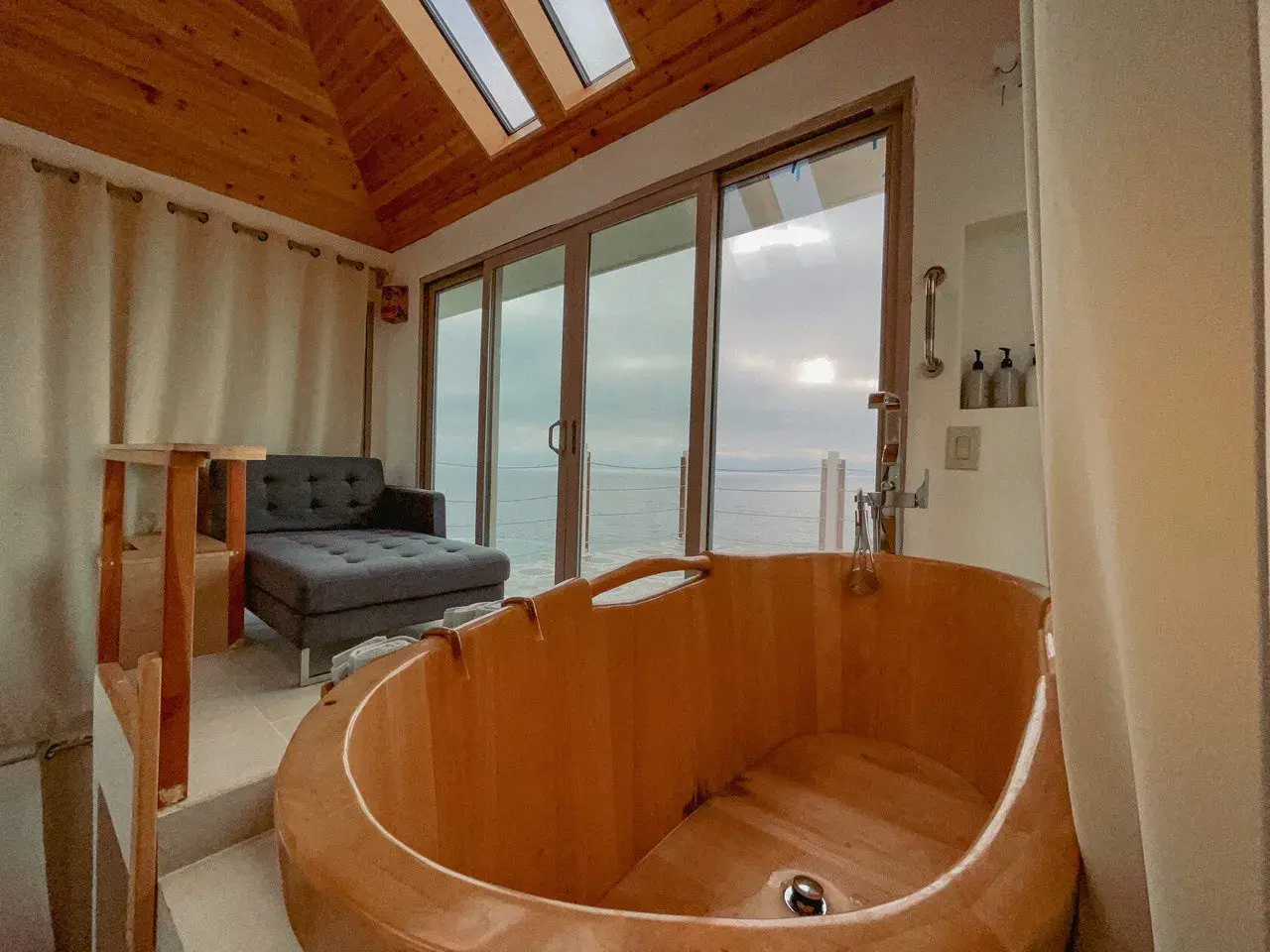 За панарамными окнами вид на океан, кресло и деревянная ванна для проведения процедур